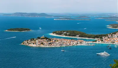 A picturesque view of a coastal town on a small island surrounded by turquoise waters, with nearby islands and boats in the distance.